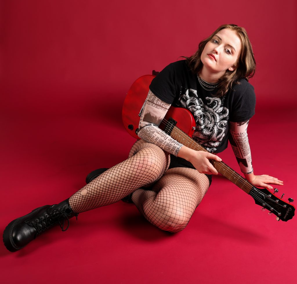 Musician In Red Musician Alicia Neil poses with her guitar on a red seamless paper backdrop.